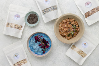 Three bowls of bircher muesli with various toppings and two packets of muesli mix, one with a rose and cardamon topping, and another with a mango and coconut topping.